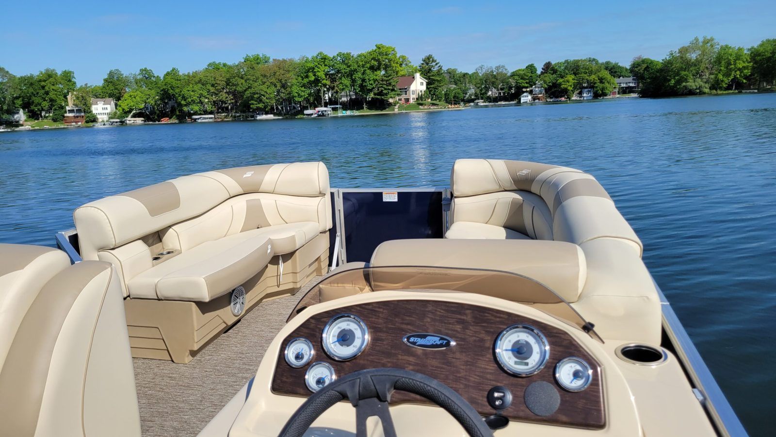 The helm and cream seating of a Golden Boat pontoon on a bright blue lake