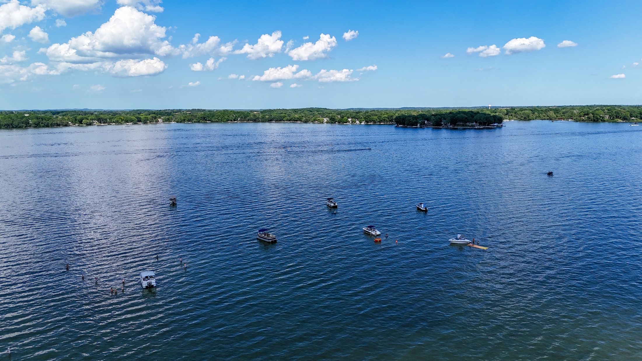 Pontoon boats spread across a bright blue Okauchee Lake on a sunny summer afternoon